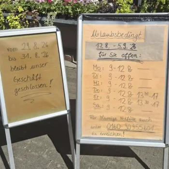 Zwei Aufsteller vor einem Blumengeschäft. Das linke Schild weist auf eine Geschäftsschließung vom 29.8. bis 31.8.2026 hin. Das rechte Schild zeigt die urlaubsbedingten Öffnungszeiten vom 17.8. bis 5.9.2026: Montag bis Mittwoch sowie Samstag von 9 bis 12 Uhr, Donnerstag und Freitag von 9 bis 12 Uhr und 13:30 bis 17 Uhr. Zudem ist die Telefonnummer 0160-90955601 für blumige Notfälle angegeben.
